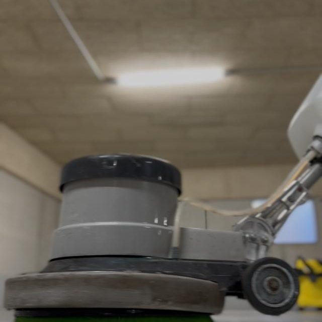 Tiefgaragenreinigung Stade Bodenreinigungsmaschine auf einem betonierten Boden in einem gut beleuchteten Raum.