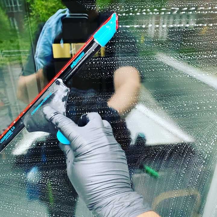 Fensterputzer Stade Eine Hand mit einem Fensterreiniger wischt über eine nasse Glasscheibe.